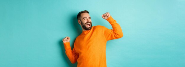 幸せな男が勝者の勝利のような腕を上げると水色の背景の上に立って祝う