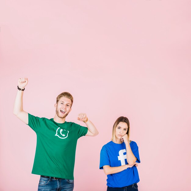 Happy man raising his arms beside upset woman on pink background