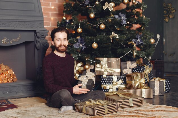 Happy man in red sweater. Guy in front of the fireplace. Male on the background of Christmas tree.