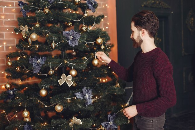 赤いセーターで幸せな男。暖炉の前の男。クリスマスツリーの背景に男性。