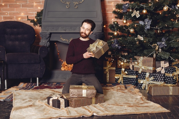 Free photo happy man in red sweater. guy in front of the fireplace. male on the background of christmas tree.