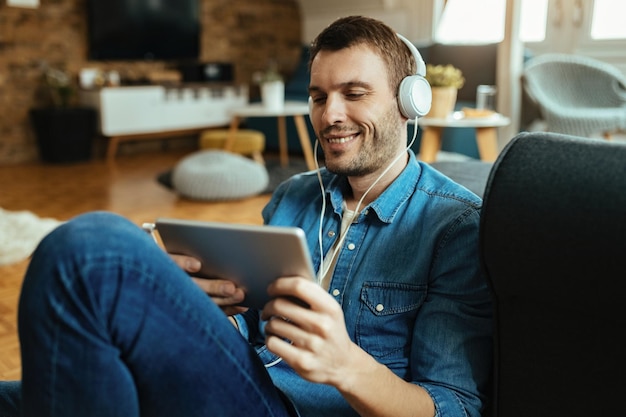 Happy man relaxing at home while using touchpad and listening music over headphones