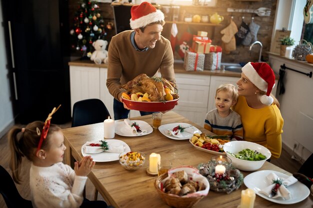 집에서 크리스마스 점심을 위해 가족에게 칠면조를 채운 행복한 남자