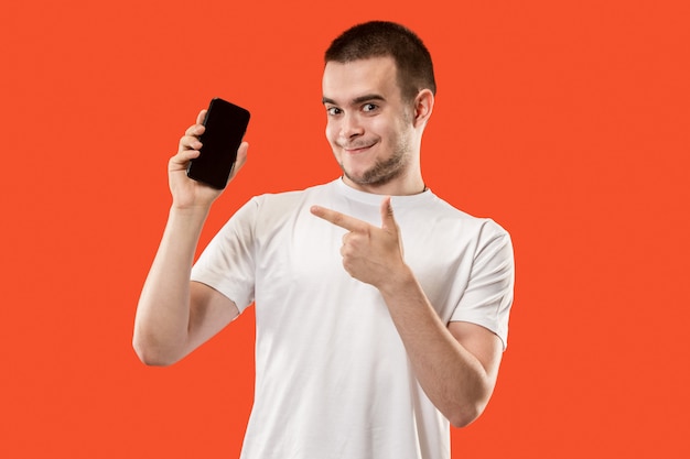 Счастливый человек показывая на пустом экране мобильного телефона против оранжевой стены