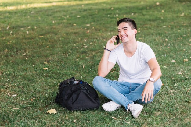 Happy man sitting on green grass talking on smartphone