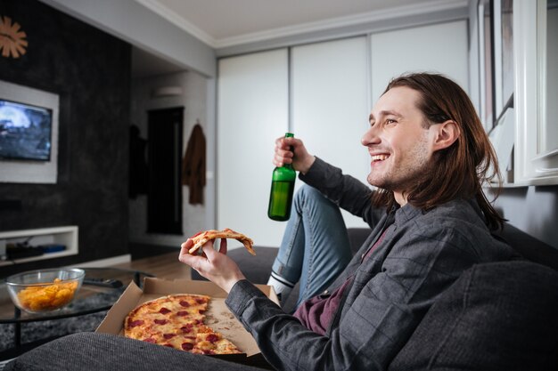 Happy man sitting at home indoors eating pizza