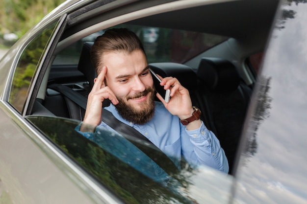 Happy man sitting inside car talking on smartphone