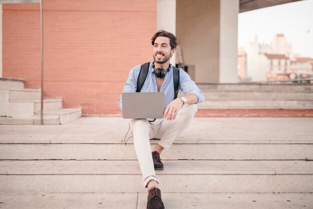 Happy man sitting on staircase with laptop