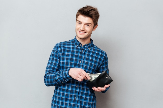 Happy man standing over grey wall holding purse with money.