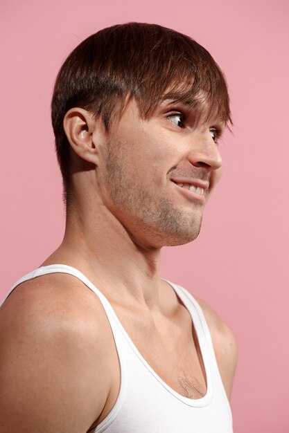 The happy man standing and smiling against pink wall.