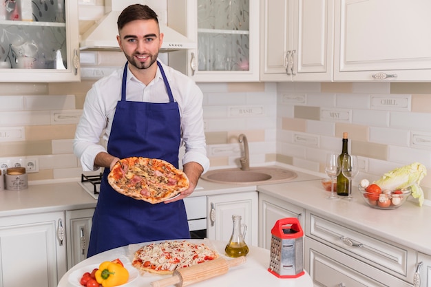 Счастливый человек, стоящий с пиццей на кухне