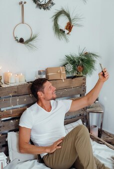 クリスマス​の​装飾​が​施された​家​で​携帯​電話​で​フォロ​を​取っている​幸せな​男​。​家族​の​オンライン​の​矛盾​。