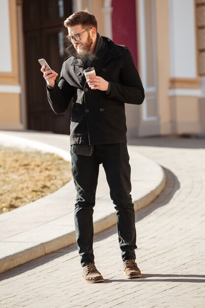 Happy man using cell phone and drinking coffee in city