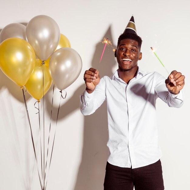 Happy man wearing party hat and holding sparklers