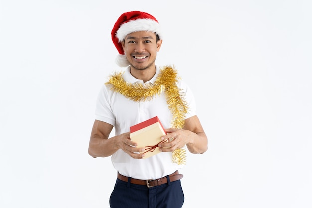 Happy man wearing Santa hat, tinsel and holding gift box