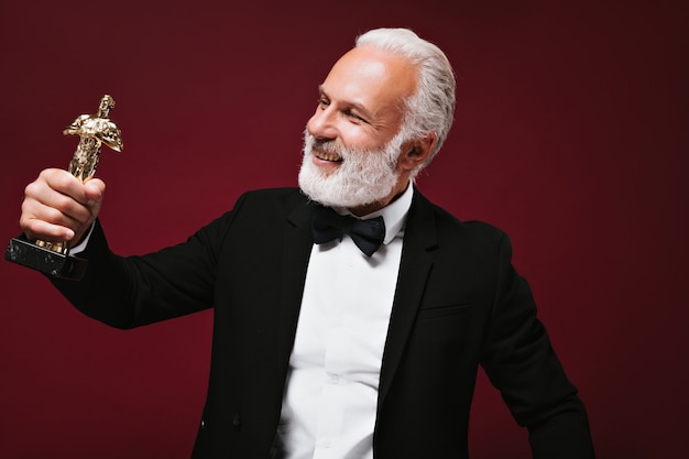 Happy man in white shirt and jacket looks at Oscar statuette