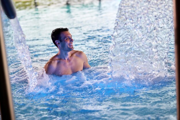 Счастливый мужчина с закрытыми глазами наслаждается крытым бассейном в спа-салоне
