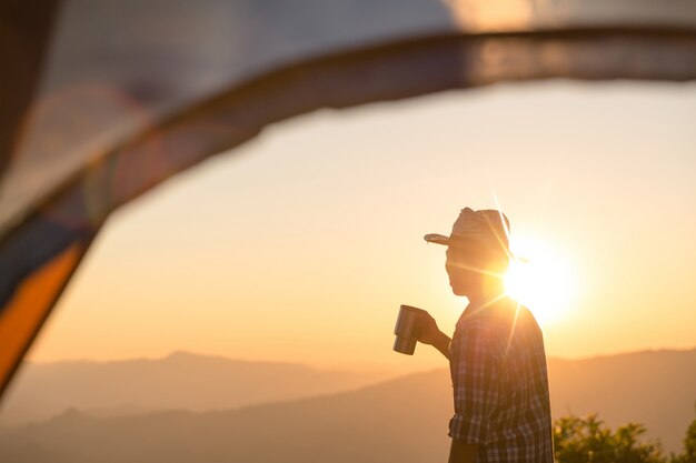 Happy man with holding coffee cup stay near tent around mountains