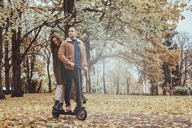 幸せな男と女は黄金の秋の公園でスクーターに乗って素敵です。