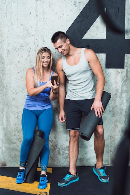 Happy man and woman looking at cellphone in gym