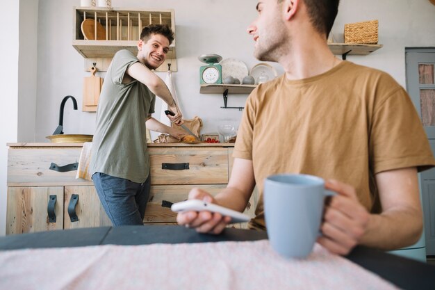 Happy man working in kitchen looking at his friend using mobile phone