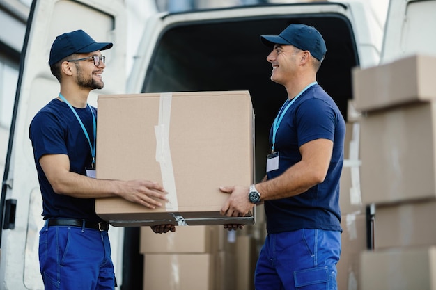 Happy manual worker cooperating while carrying cardboard boxes in a delivery van