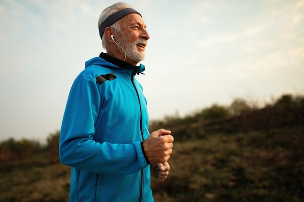 Free photo happy mature athlete running in the morning in nature and listening music on earphones copy space