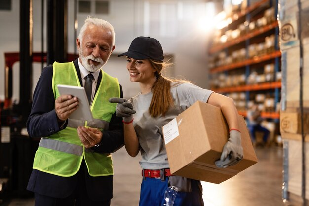 Happy mature businessman and female worker using digital tablet in industrial storage compartment
