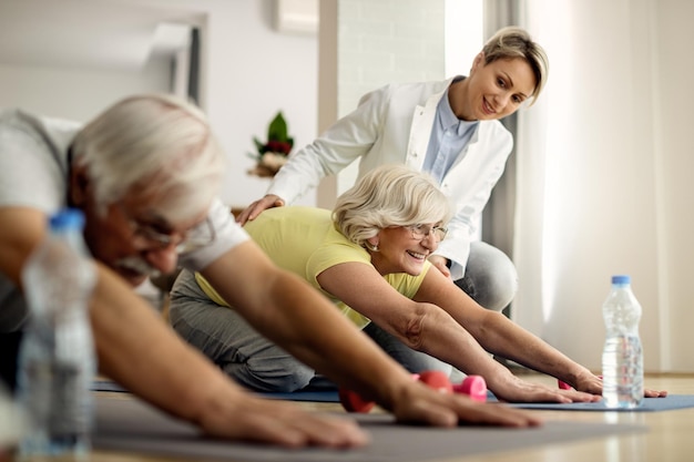 Happy mature couple doing stretching exercises with help of physiotherapist at home