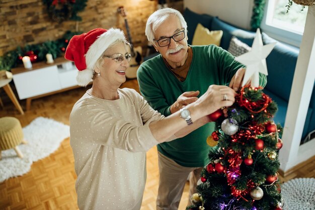 Happy mature couple preparing for Christmas and decorating the tree at home