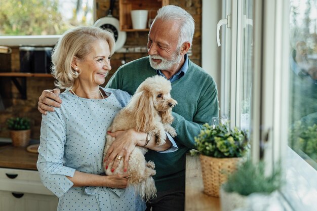 Happy mature couple with a poodle enjoying by the window