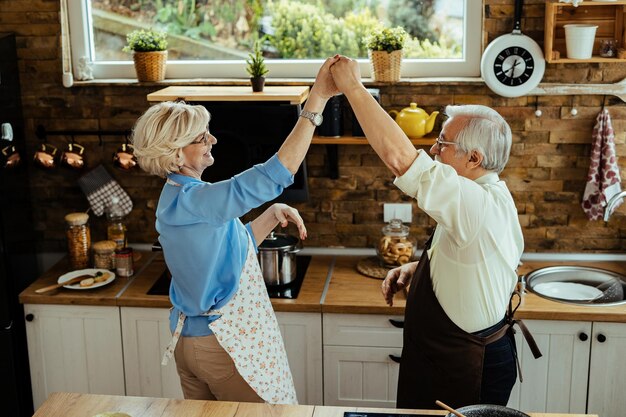 キッチンで踊りながら楽しんで幸せな成熟した夫と妻