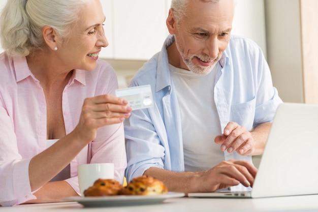Happy mature loving couple family using laptop holding credit card
