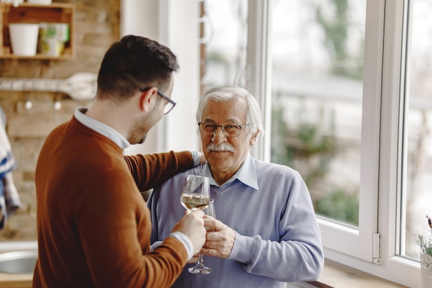 Foto gratuita felice uomo maturo e suo figlio adulto che bevono vino e parlano in cucina