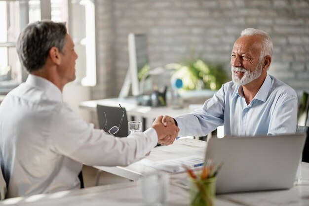 Happy mature man and his financial advisor shaking hands after the meeting in the office