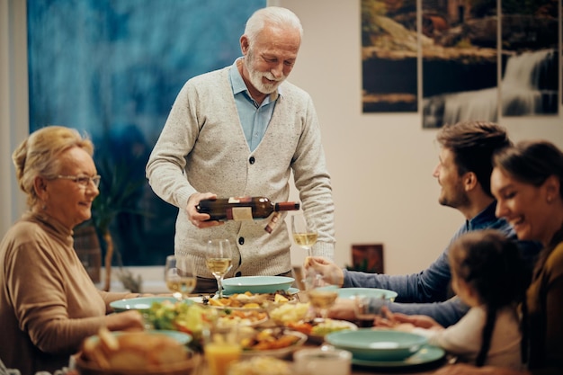 Счастливый зрелый мужчина, подающий вино во время семейного обеда в столовой