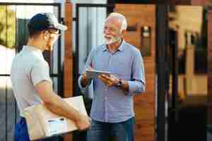 Free photo happy mature man signing on digital tablet for a delivery while communicating with a courier