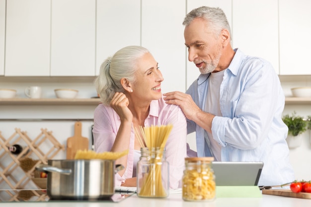 Happy mature man standing near mature cheerful woman using tablet