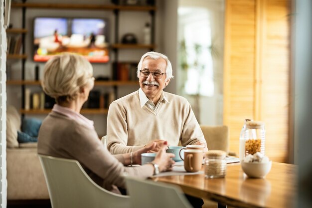 朝の食卓で朝食を食べながら妻と話している幸せな成熟した男