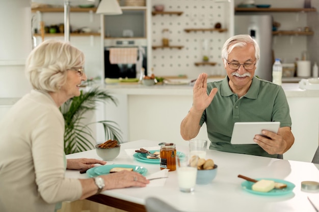 Free photo happy mature man waving while making video call over digital tablet at home