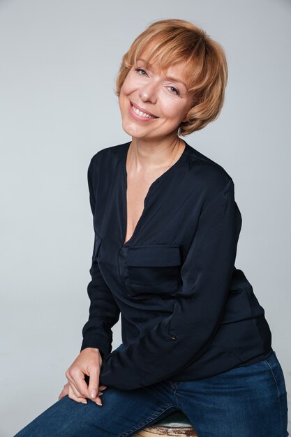 Happy mature woman sitting and posing isolated