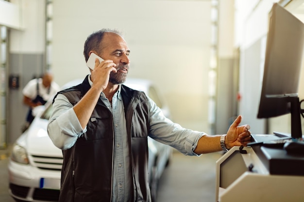 Happy mechanic talking on the phone while using computer at auto repair shop