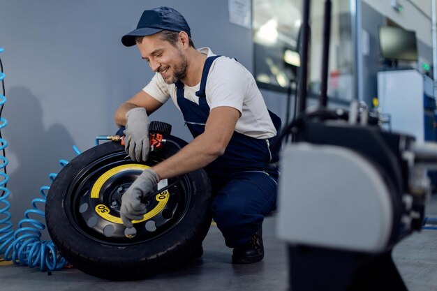 Happy mechanic using pressure gauge while repairing car tire in a workshop