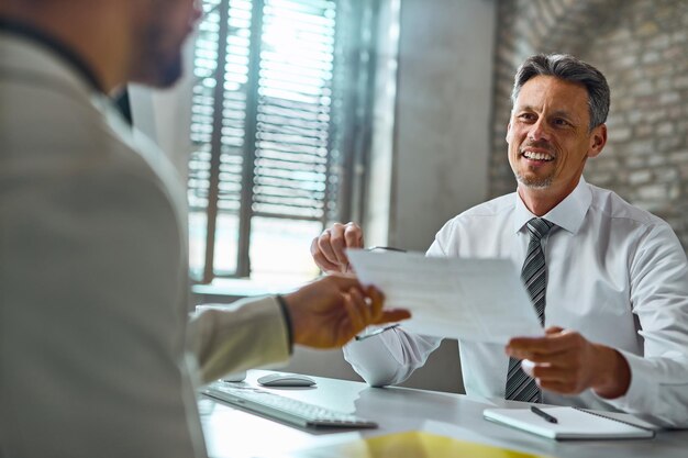 Happy mid adult businessman talking with a candidate and taking his resume during job interview in the office