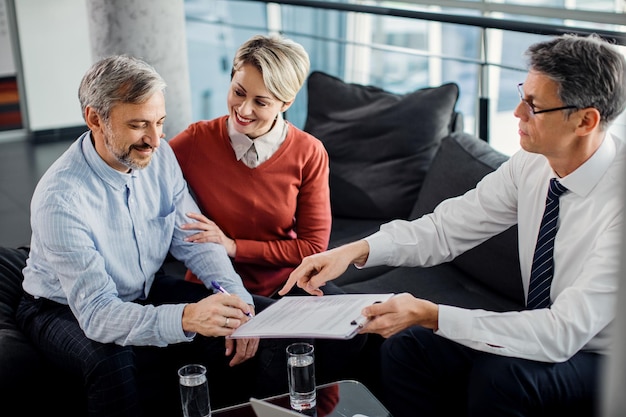 Happy mid adult couple signing a contract with their agent in the office