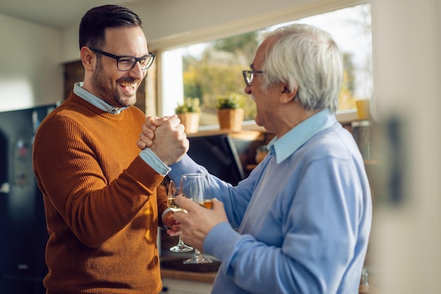 Счастливый взрослый мужчина и его старший отец держатся за руки, приветствуя друг друга на кухне
