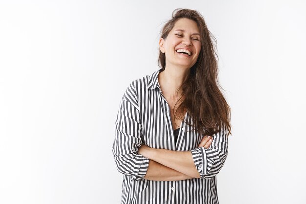 Happy middle-aged laughing sincerely close eyes and cross hands over chest having fun amused with lovely gift children made, chuckling joyfully as posing in striped blouse over white wall