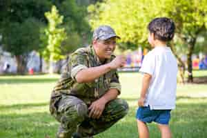 무료 사진 선교 여행 후 아들과 함께 행복한 군사 아버지 모임. 공원에서 위장 유니폼을 입고 아빠에 게 걷는 소년. 가족 상봉 또는 귀국 개념