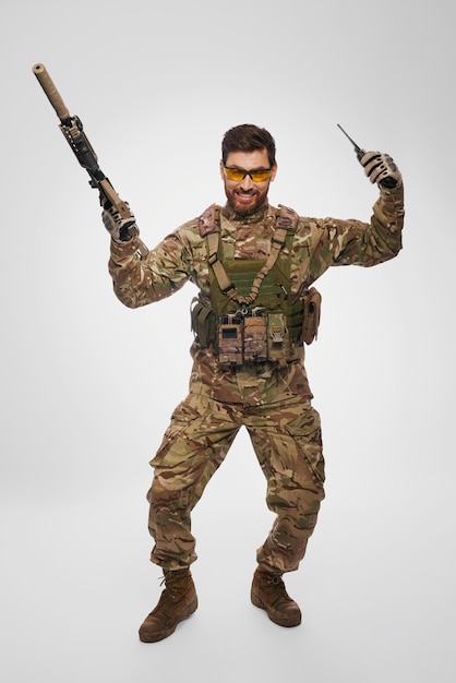 Free photo happy military infantryman jumping with raised arms and rejoicing in studio front view of cheerful