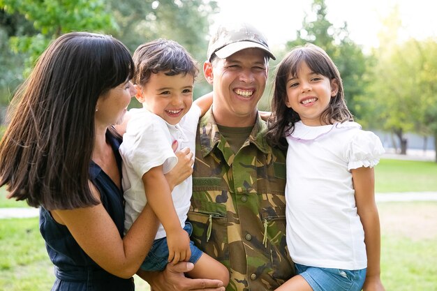 그의 가족과 함께 포즈를 취하는 행복한 군인, 팔에 아이를 안고, 그의 아내는 모두 포옹하고 웃고. 미디엄 샷. 가족 상봉 또는 귀국 개념